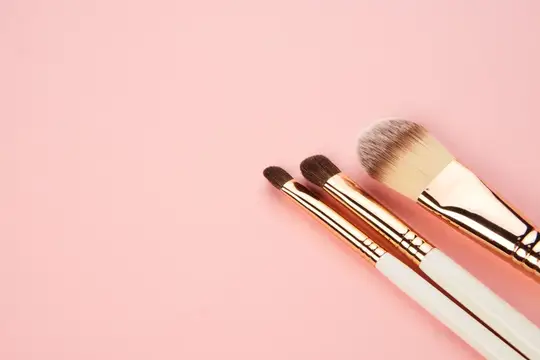Три кисти для макияжа с золотистыми ручками на розовом фоне