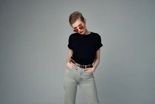 Стильная девушка с короткой стрижкой в красных очках на сером фоне