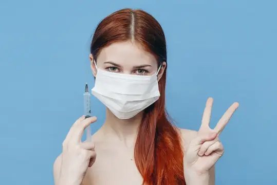 Женщина в медицинской маске держит в руке шприц, обнаженные плечи, инъекция ботокса