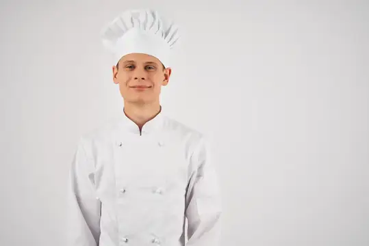Молодой повар в белом колпаке и кителе на светлом фоне