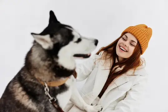 Улыбающаяся девушка в жёлтой шапке с хаски на зимней прогулке