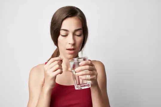 Молодая женщина держит стакан воды и собирается принять таблетку