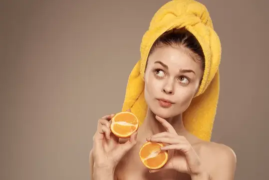 Женщина с полотенцем на голове, обнаженными плечами и цитрусовыми фруктами в руках занимается уходом за кожей