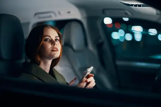 Рыжеволосая женщина с телефоном в салоне автомобиля ночью