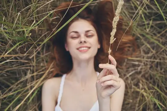 Женщина в белом платье лежит на траве, подняв руки вверх, веселится