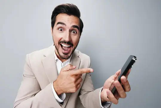 Удивлённый мужчина в бежевом пиджаке показывает на смартфон