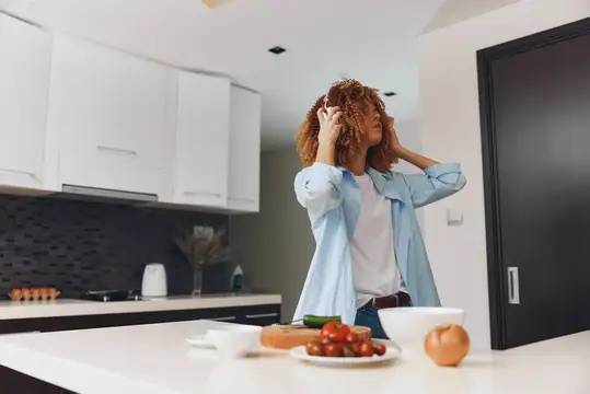 Кудрявая женщина в голубой рубашке танцует на кухне