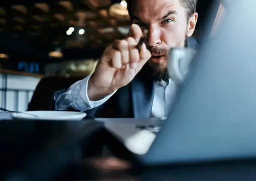 Сосредоточенный бородатый мужчина в костюме смотрит на экран ноутбука