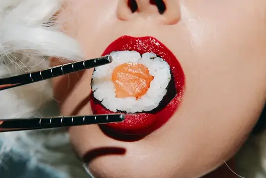 Красные губы крупным планом держат суши палочками