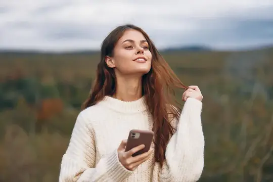 Молодая женщина в белом свитере с телефоном на осенней прогулке