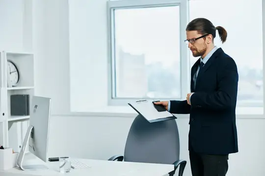 Мужчина с хвостом и в очках читает документы в офисе