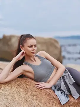 Молодая женщина в спортивной одежде отдыхает на камне у моря