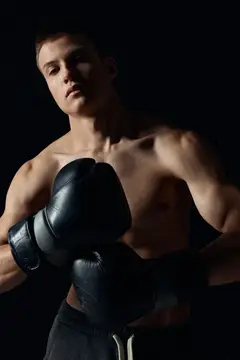 Молодой боксёр в чёрных перчатках на тёмном фоне