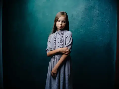 Светловолосая девочка в сером платье на тёмно-бирюзовом фоне