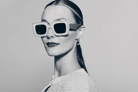 Светловолосая женщина в массивных солнцезащитных очках на сером фоне