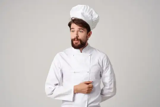 Бородатый повар в белом колпаке и кителе на сером фоне