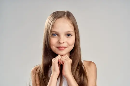 Весёлая девушка в белой футболке, улыбка, длинные волосы, крупный план, светлый фон, кадр обрезан
