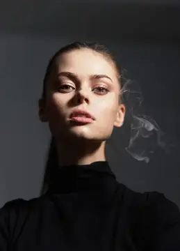 Молодая женщина с сигаретным дымом на тёмном фоне