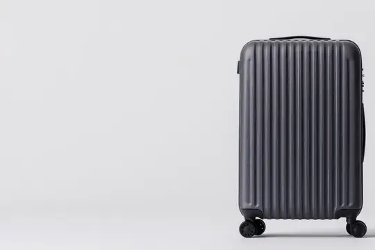 Черный пластиковый чемодан на колесах стоит на светлом фоне