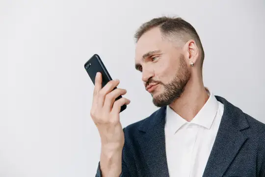 Бородатый мужчина в пиджаке слушает голосовое сообщение на смартфоне