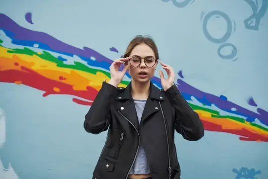 Женщина в кожаной куртке стоит на улице возле стены, демонстрируя современный модный стиль