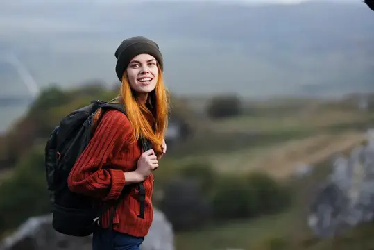 Жизнерадостная женщина-турист с рюкзаком на фоне горного пейзажа наслаждается свежим воздухом