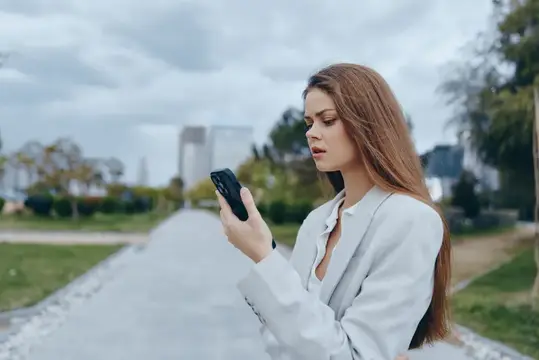 Молодая женщина с длинными волосами смотрит в телефон на улице