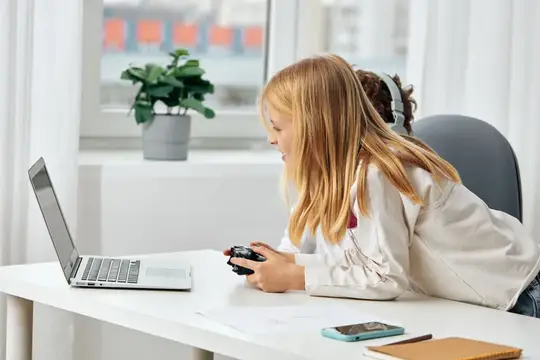 Рыжеволосая девочка в наушниках играет в игру за ноутбуком