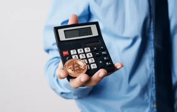 Мужчина в голубой рубашке держит калькулятор с биткоином