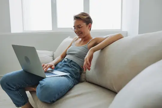 Улыбающаяся женщина с короткой стрижкой работает за ноутбуком на диване