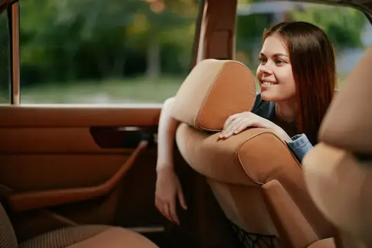 Улыбающаяся девушка выглядывает из окна автомобиля на природе