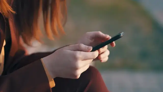 Рыжеволосая девушка держит смартфон в руках на улице