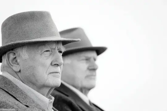 Двое пожилых мужчин в стильных шляпах запечатлены в момент созерцания, демонстрируя задумчивые выражения лиц в спокойной черно-белой атмосфере, символизирующей размышления и мудрость