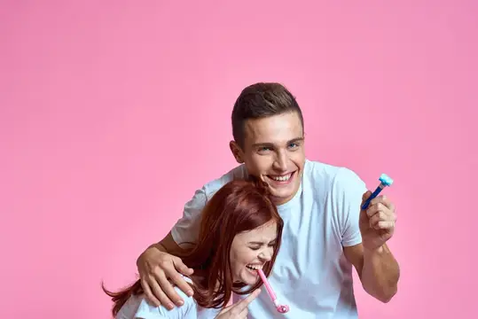 Молодая пара с зубными щетками смеется на розовом фоне