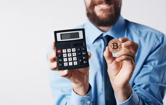 Улыбающийся бородатый мужчина в рубашке держит калькулятор и биткоин