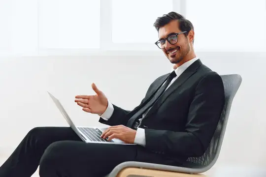 Улыбающийся мужчина в очках и костюме работает за ноутбуком в светлом офисе