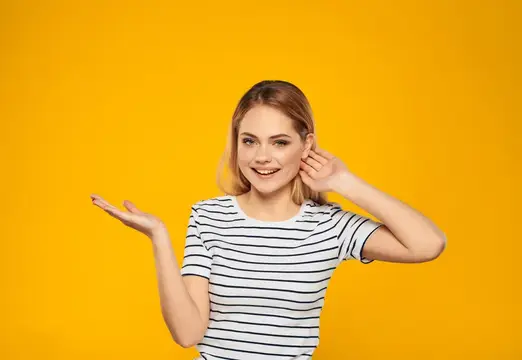 Улыбающаяся блондинка в полосатой футболке жестикулирует на жёлтом фоне