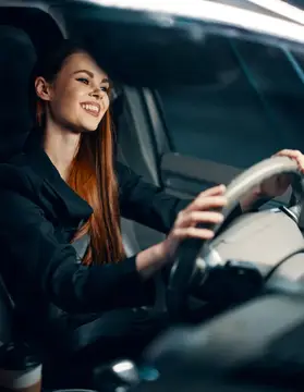 Улыбающаяся рыжеволосая девушка за рулём автомобиля