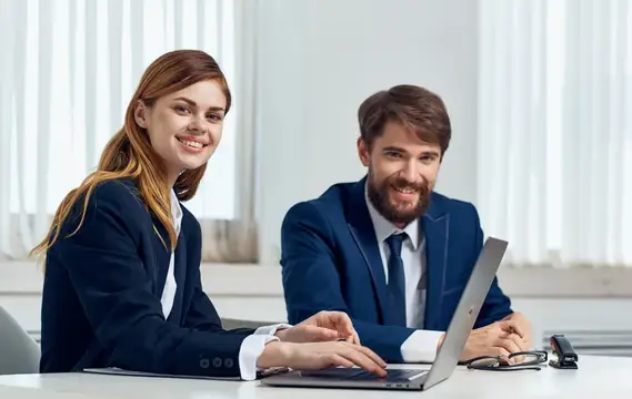 Улыбающиеся мужчина и женщина в офисах работают за ноутбуком