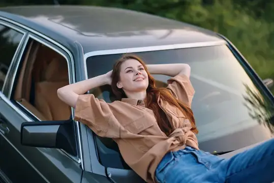 Рыжеволосая девушка отдыхает на капоте серого автомобиля