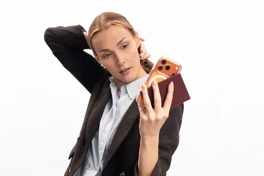 Молодая женщина в коричневой куртке пользуется смартфоном, чтобы сделать селфи, позируя с рукой за головой