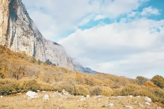 Осенний горный склон с отвесной скалой в облаках