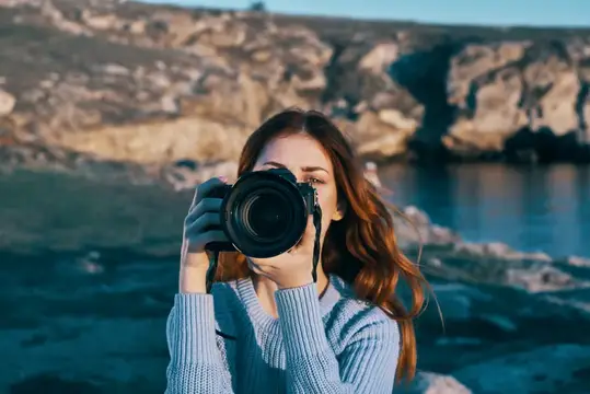 Молодая женщина фотографирует на камеру у скалистого берега