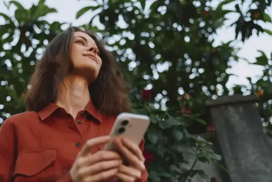 Непринужденная сцена на открытом воздухе с женщиной и телефоном, передающая досуг, природу и полное надежды настроение при ярком дневном свете в контексте стиля жизни и благополучия