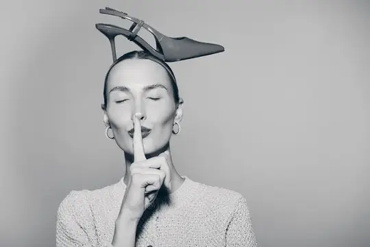 Девушка с туфлей на голове прикладывает палец к губам