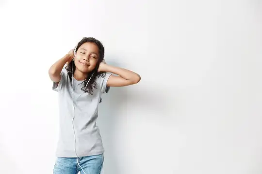 Улыбающаяся темноволосая девочка в наушниках на белом фоне