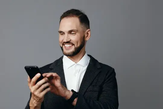 Улыбающийся бородатый мужчина в пиджаке смотрит в смартфон