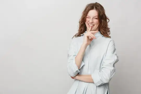 Счастливая кудрявая женщина в белой блузке делает жест «тихо», прикладывая палец к губам