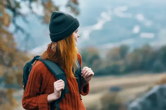 Весёлая женщина-туристка с рюкзаком путешествует по осенним горам
