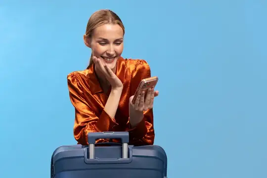 Улыбающаяся женщина с телефоном стоит за синим чемоданом